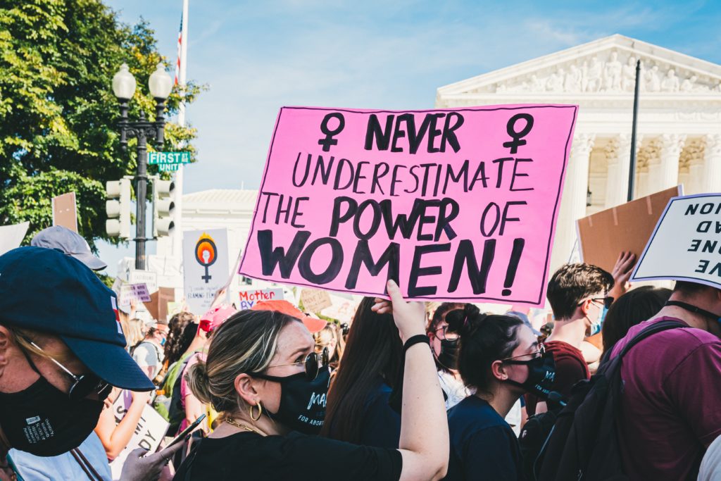 photo shows womens' rights march. Banner reads "never underestimate the power of women"